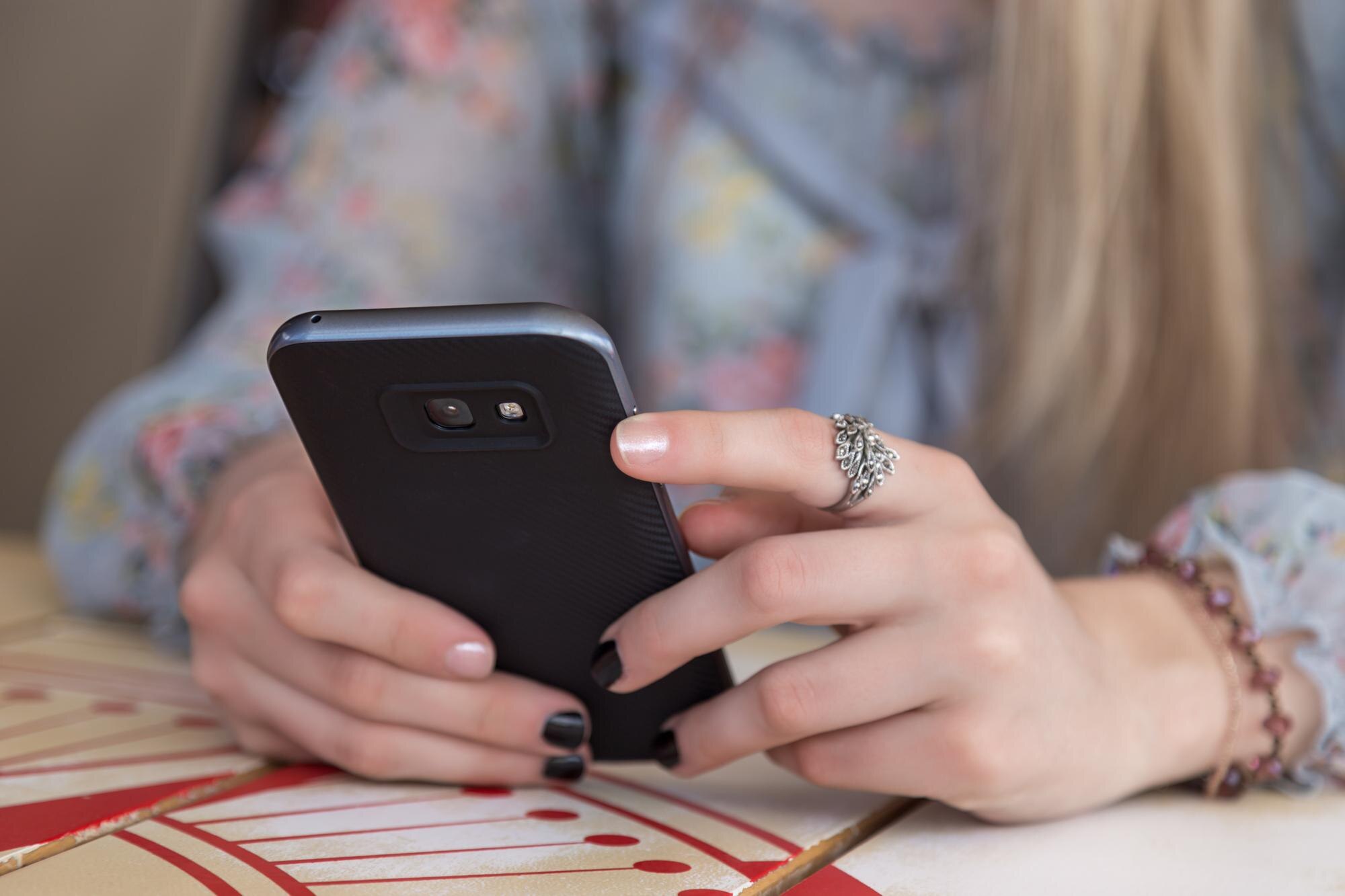 Środkowa część kobiety używającej telefonu komórkowego przy stole