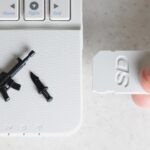 Przycięta ręka trzymająca kartę pamięci przy laptopie przy biurku