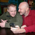Ojciec i syn komunikują się, siedząc przy stole i studiują informacje na telefonach