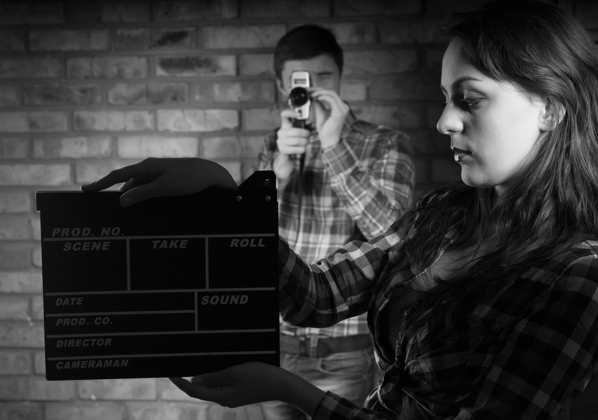 Poważna młoda kobieta trzyma deskę klapy z młodym fotografem z tyłu. Uchwycone w trybie monochromatycznym.