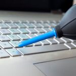 Bliska strzał kobiecej dłoni zamiatania kurzu z klawiatury laptopa za pomocą żarówki powietrza