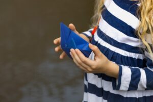 Dziewczyna trzyma w rękach niebieską papierową łódkę w kałuży po deszczu, lato