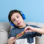8-letnie dziecko ze słuchawkami i trzymające kolorowego lizaka robiące śmieszną minę.