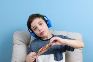 8-letnie dziecko ze słuchawkami i trzymające kolorowego lizaka robiące śmieszną minę.