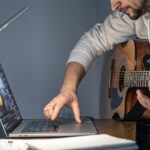 Mężczyzna z gitarą przed laptopem o późnej porze uczy się grać
