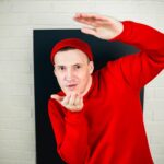 Mężczyzna w czerwonym kapturze i kapeluszu tańczy na białą ceglaną ścianę