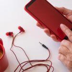 Kobiece ręce używające telefonu z czerwonym ekranem Biały pulpit z filiżanką kawy i słuchawkami