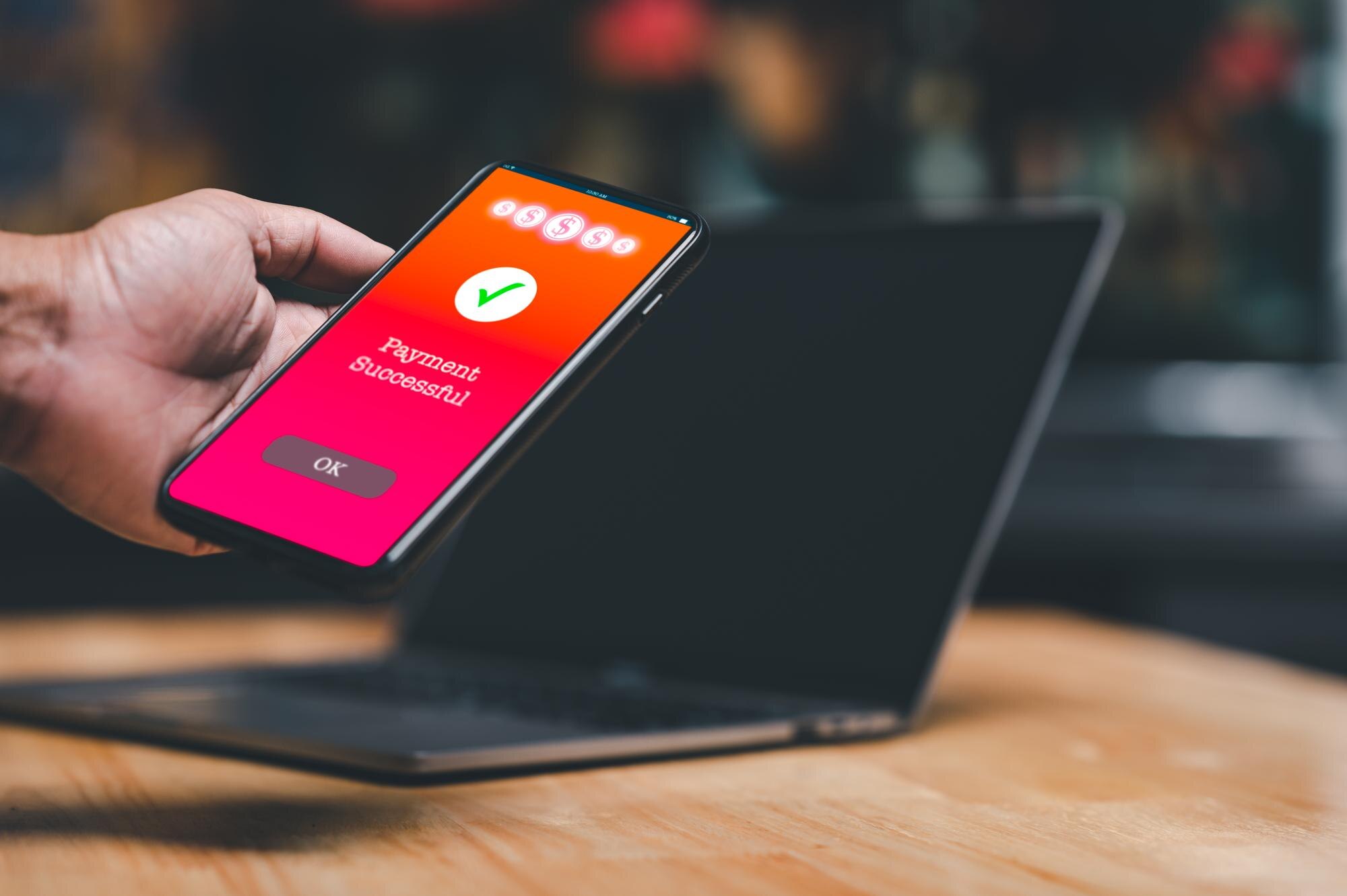 Osoba trzyma w ręku telefon komórkowy z napisem "Płatność zakończona"