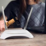 Ręka z młotkiem i routerem z modemem internetowym