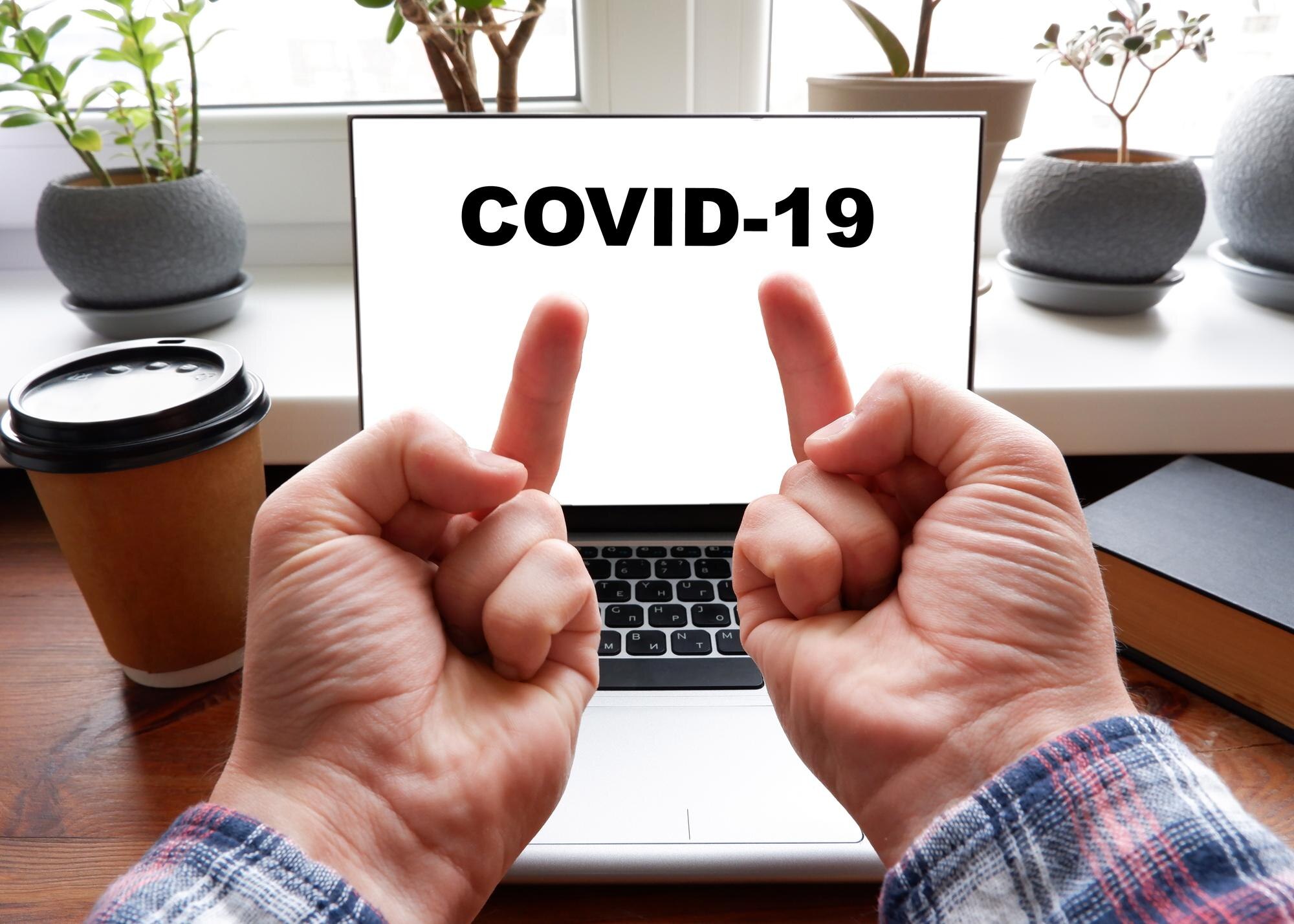 Mężczyzna pokazuje dwuręcznego pieprzenia na ekranie laptopa, na ekranie którego jest napisane COVID19