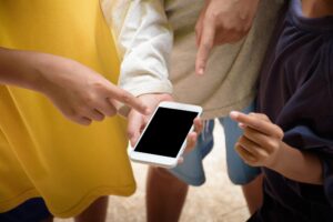 Ręka trzymająca czarny ekran smartfonu i wiele rąk wskazujących na ekran telefonu komórkowego zbliżenie w miękkim świetle słonecznym rozmyte tło koncepcja mediów społecznościowych i komunikacji dla projektowania i makiety