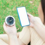 Zrobione od tyłu przez ramię rozmazanej Azjatki Ale oczywiście telefon komórkowy, który przycina ekran na biało i kompas Usiądź w mediach społecznościowych i znajdź wskazówki w parku