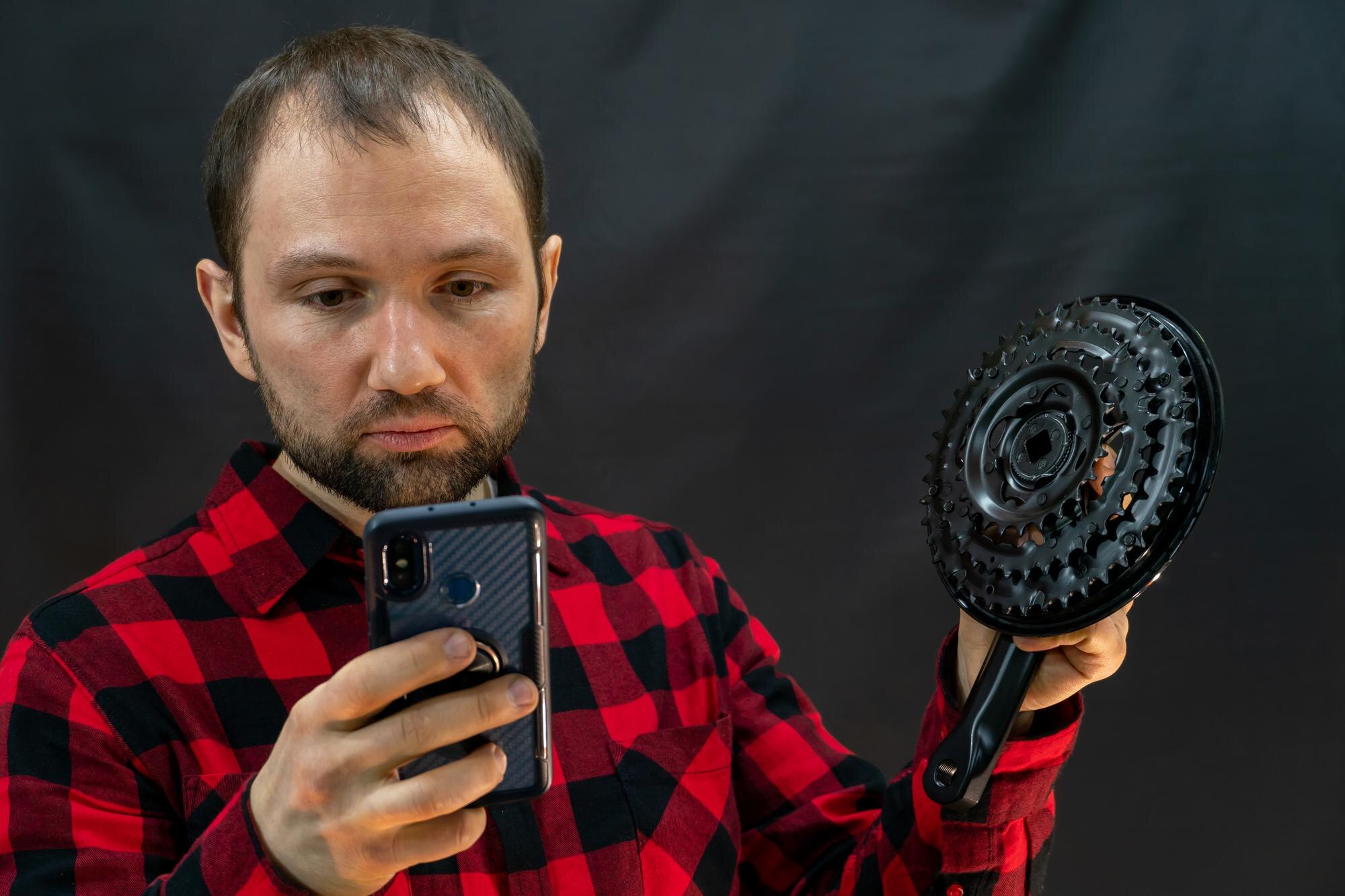Młody mechanik rowerowy w czerwonej koszuli w kratę z częściami rowerowymi w dłoniach stoi na czarnym tle Nowy mechanizm korbowy jest w rękach mechanika Naprawa rowerów