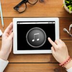 koncepcja technologii, ludzi i multimediów - zbliżenie kobiety z ikoną odtwarzacza multimedialnego muzyki na ekranie komputera typu tablet pc na drewnianym stole