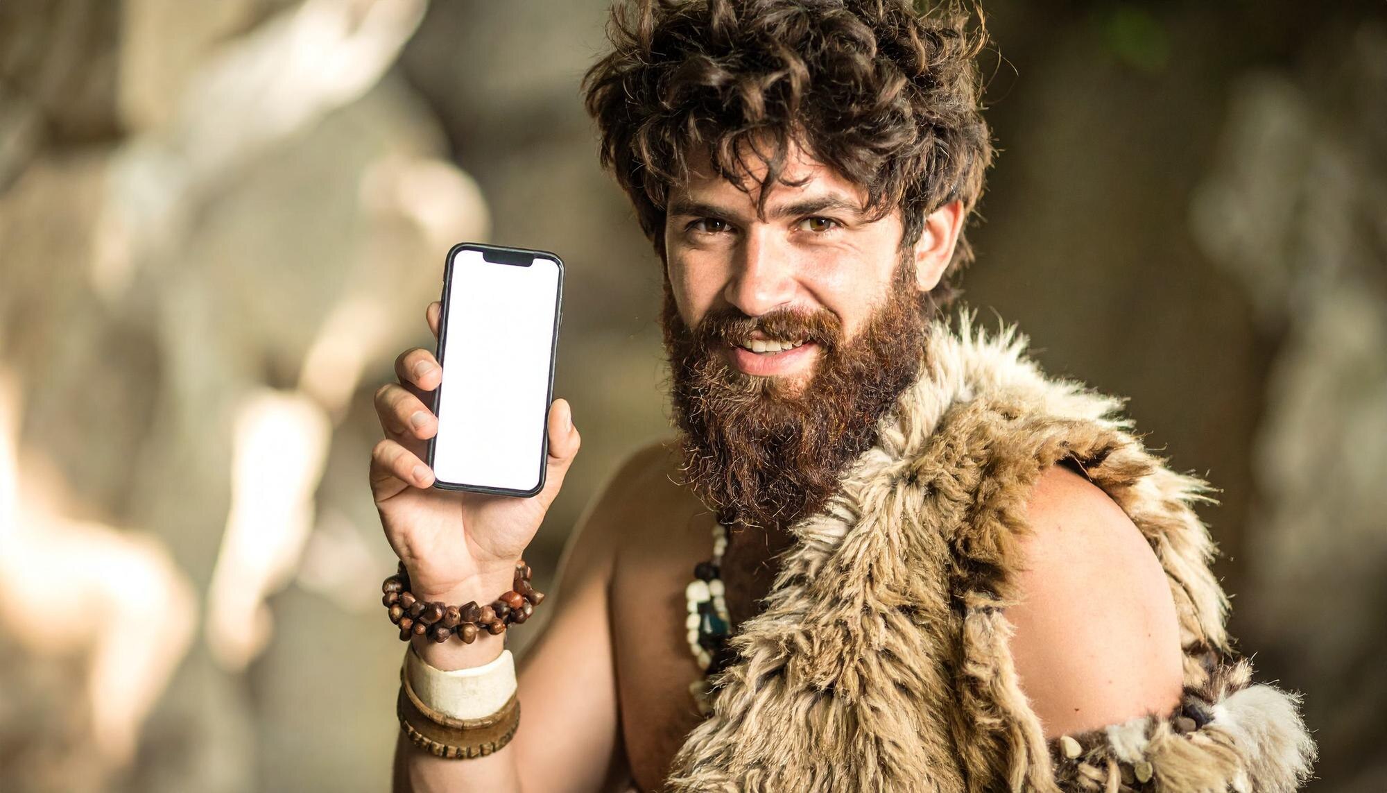 Caveman holding smartphone in a natural setting during the stone age era
