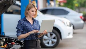 Focused professional using a laptop to check information beside a car at a service station