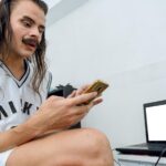 Młoda, niebinarna osoba z Ameryki Łacińskiej korzystająca z telefonu komórkowego w swojej sypialni