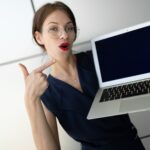 Piękny pracownik biurowy pokazuje gest na pustym ekranie laptopa